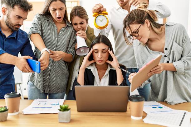 2.estrés laboral. Una mujer sentada en una mesa y un grupo de personas hablándole al mismo tiempo.